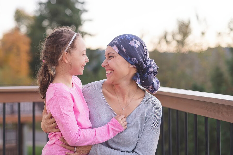 Woman wearing a headscarf holding a young child and smiling at each other outdoors.